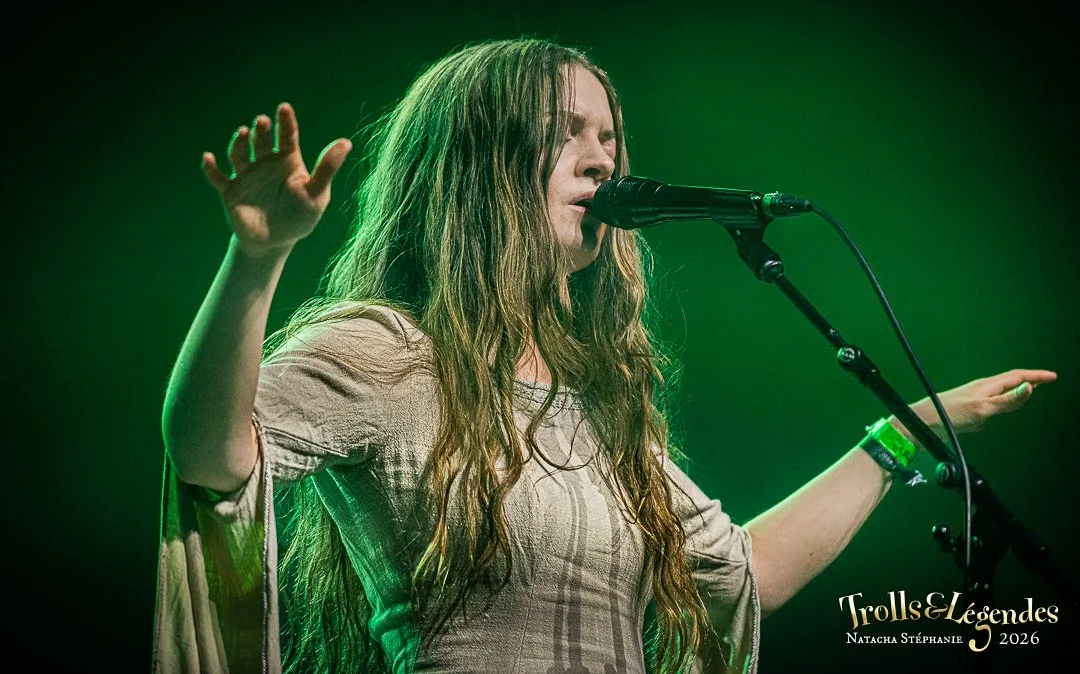 KALANDRA en concert: une chanteuse aux longs cheveux, robe légère, bras levés. Micro devant elle, lumière verte éclaire la scène dans l’ambiance du hub Concerts pour le Festival 2026.