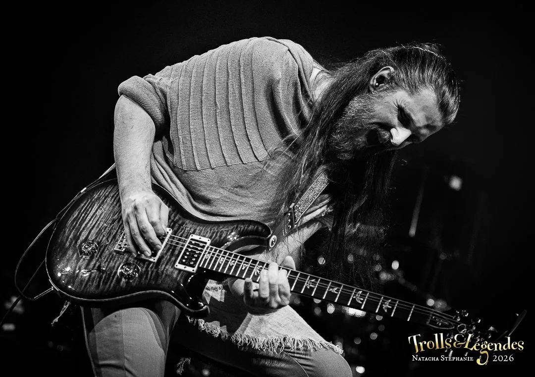 Kalandra sur scène : guitariste à longue chevelure et barbe, vêtement tricoté fluide, manie une guitare électrique sombre avec virtuosité. Ambiance sombre et intense, festival 2026, hub Concerts.